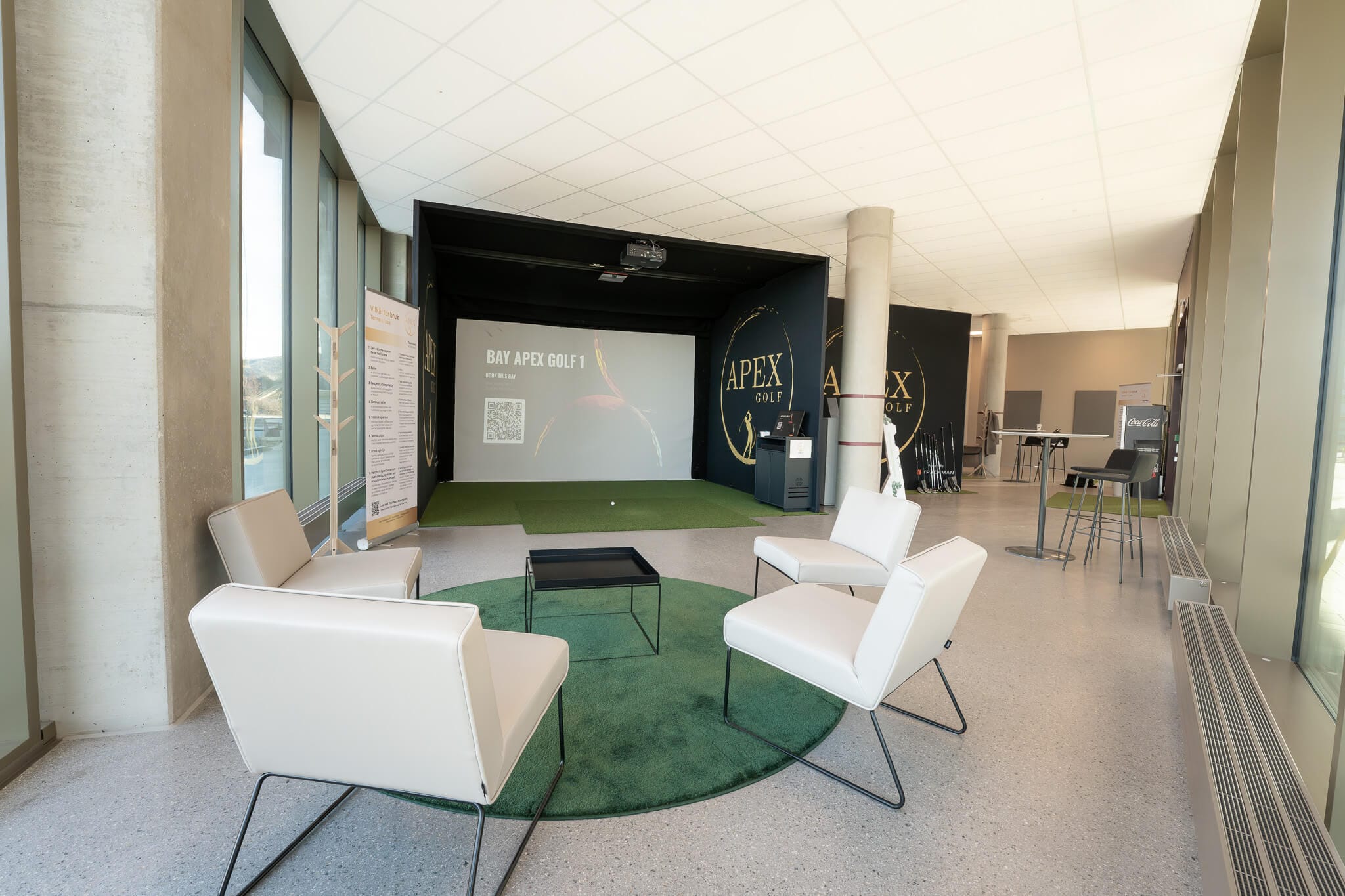 Den moderne innendørs simulatorsonen hos Apex Golf Hinna Park, utstyrt med TrackMan iO-sensor i taket, grønn gressmatte og en koselig loungesone for spillere.