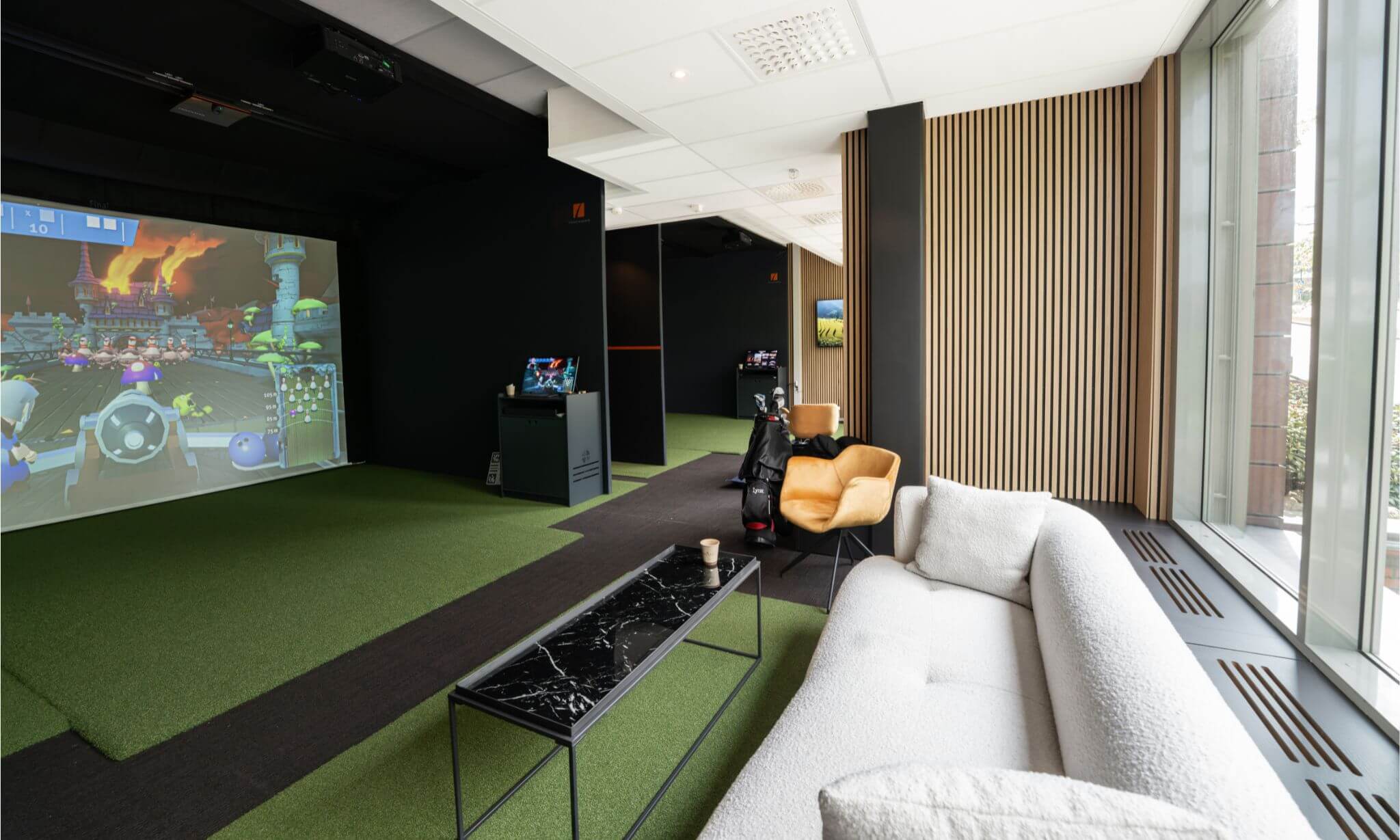 Innendørsutsikt fra Apex Golf Smedvigkvartalet. Bildet viser to utslagssteder ved siden av hverandre med TrackMan iO-sensorer i taket og store simulatorskjermer.