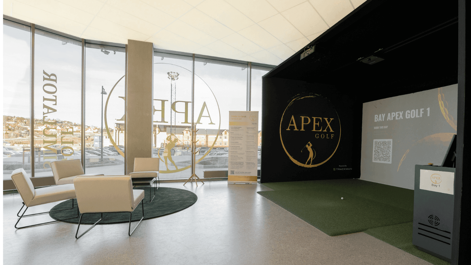 Interiør fra Apex Golf Hinna Park som viser en innendørs simulatorsone utstyrt med TrackMan iO-sensor i taket, grønn gressmatte og lerret.